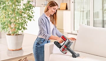 The image shows a girl who vacuums the sofa with the portable Polti Forzaspira D-Power SR550