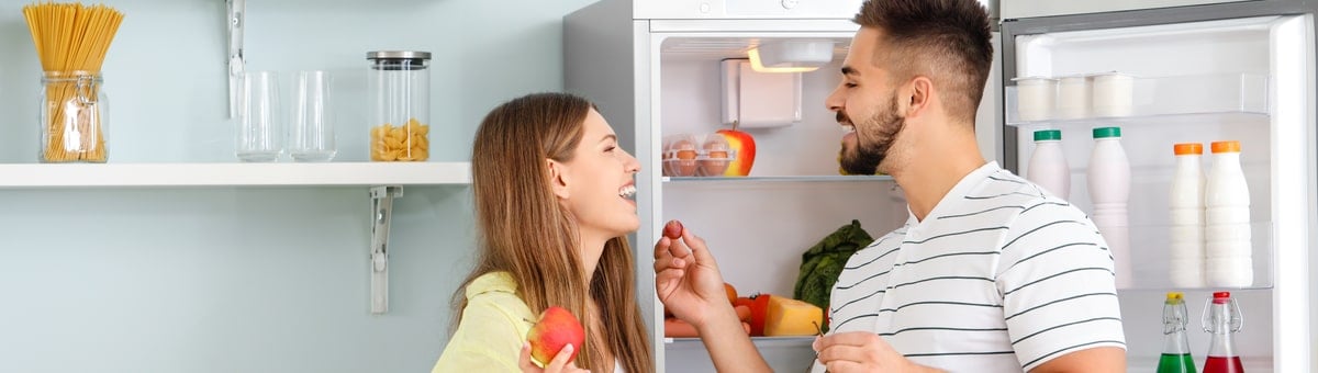 paar seisab köögis külmkapi juures ja sööb puuvilju