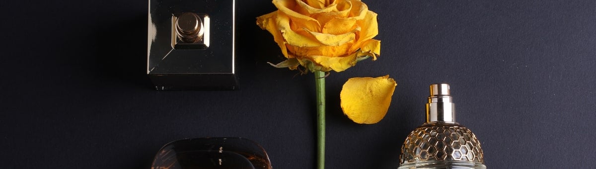 kolm unisex parfüümi ja kollane roos mustal laual