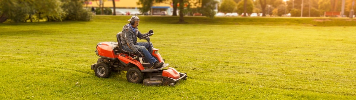 мужчина с садовым трактором косит траву во дворе