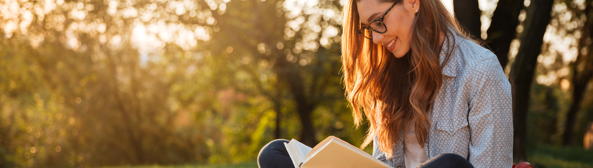 brünett prillidega naine istub pargis pingil ja loeb raamatut